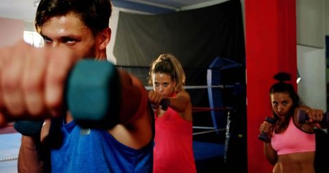Intense group boxing workout reaching forward with dumbbells, focused gym training