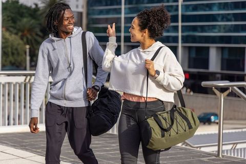 Diverse friends walking and chatting in athleisure carrying gym duffel bags in city