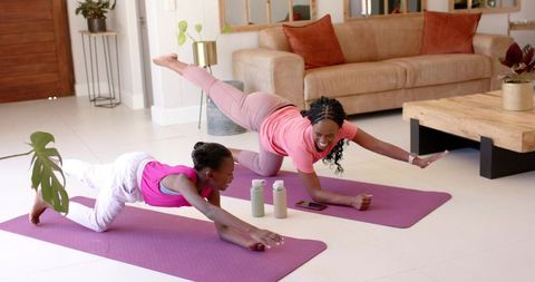 African american mother daughter practicing at-home yoga balance on purple mats