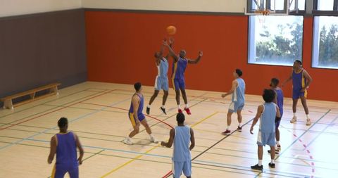 Diverse male basketball players jumping in school gym