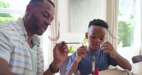 African american father teaching son painting at home table bonding and creative learning