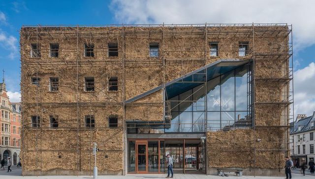 Four-story vine-clad building with scaffolding and glass entrance on urban plaza