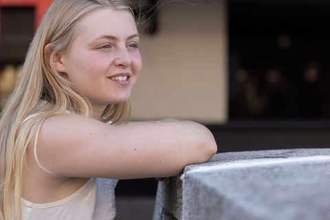 Young woman leaning on stone ledge smiling, casual urban portrait in soft daylight