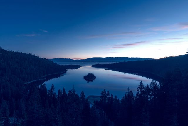 This image captures a serene sunrise over Lake Tahoe, with calm water reflecting the early morning sky. The view is framed by forested mountains, adding to the tranquility. Ideal for travel brochures, nature magazines, desktop wallpapers, and websites promoting outdoor activities or nature retreats.