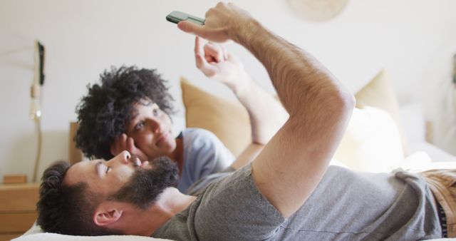 Image of happy diverse couple relaxing at home, lying on bed using smartphone - Download Free Stock Photos Pikwizard.com