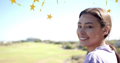 Smiling young woman looking back in sunny park with gold star garland and copy space