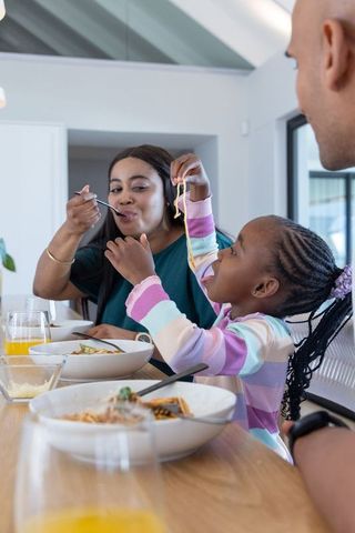 African american family enjoying spaghetti together at sunlit modern kitchen dining table
