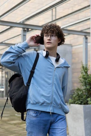 Teen student walking outdoors talking on smartphone wearing hoodie backpack headphones
