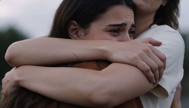 Woman crying while receiving comforting embrace from friend outdoors, emotional support