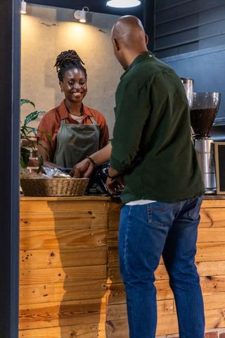 African american barista smiling while serving customer at rustic coffee shop counter