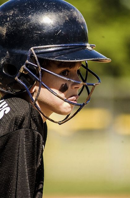 This image shows a youth baseball player wearing a helmet with protective face gear, appearing focused and determined. Ideal for articles or promotions related to youth sports, baseball training programs, or team advertisements. It captures the spirit and dedication of young athletes in action.