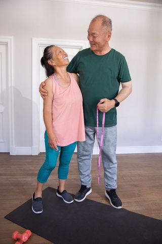 Chinese senior couple measuring fitness progress at home, smiling and embracing post workout