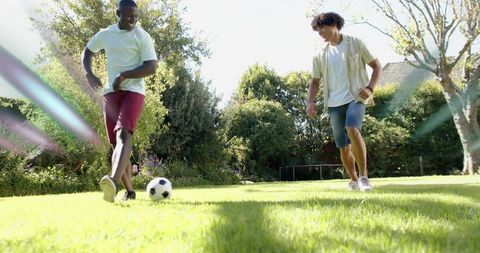 Playing backyard soccer on sunny lawn two friends kicking ball and laughing together