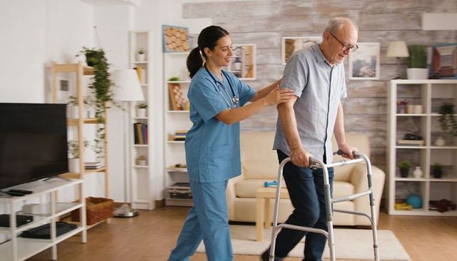 Home caregiver assisting elderly man using walker in cozy living room for mobility