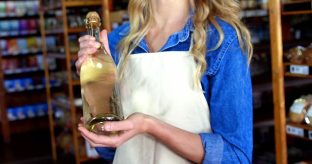 Female shop assistant holding a bottle of wine, showcasing products in an artisanal grocery store. Ideal for concepts related to small businesses, retail, local markets, customer service, and organic products. Use in promotions for local stores, blogs about retail management, and organic food marketing.