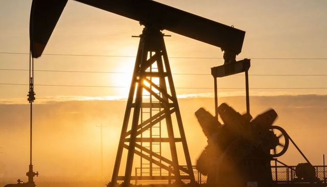 Sunrise silhouetting oil pumpjack with lattice tower and walking beam in golden haze