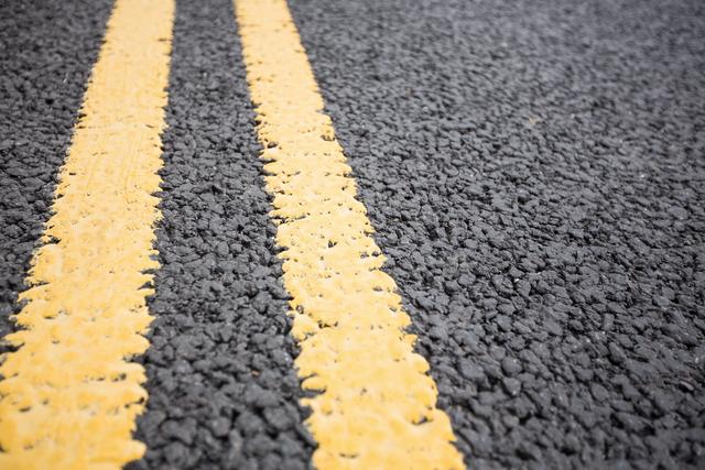 Close-up view of freshly painted yellow road markings on a textured asphalt road. Useful for backgrounds, design projects focusing on transportation and infrastructure, road safety campaigns, urban planning presentations, and driving-related articles.