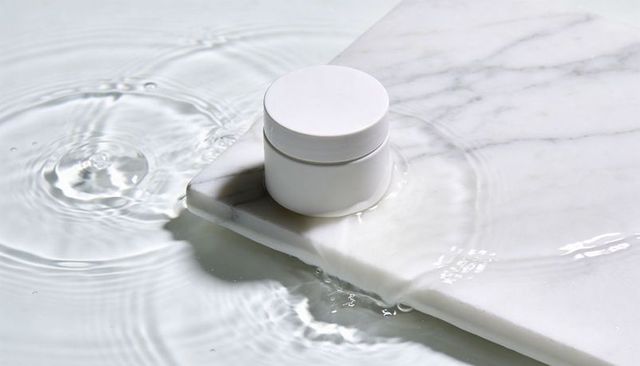 Minimal matte white cosmetic jar on marble slab with rippling water for skincare branding