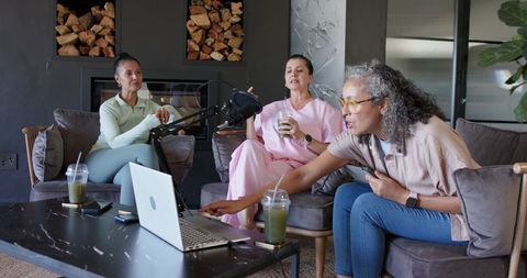 Women recording wellness podcast in lounge with laptop, microphones and green smoothies