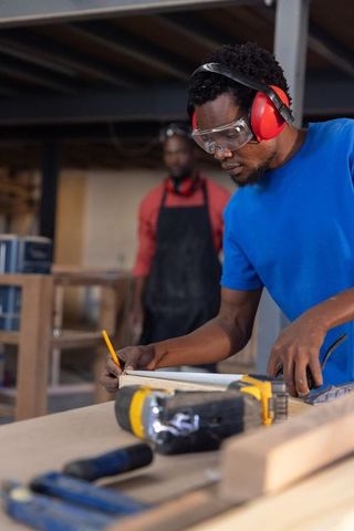 African american carpenter measuring wood with pencil and ruler in workshop