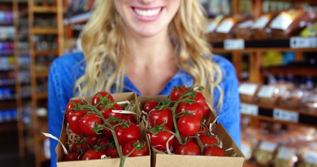 This visual showcases a cheerful woman holding boxes of fresh, organic tomatoes in a grocery store. It emphasizes healthy, local produce and shopping for nutritious food. Ideal for advertisements promoting farmers' markets, healthy eating, fresh produce, and local shopping. Can be used in blogs, marketing campaigns, and social media dedicated to healthy lifestyles and sustainable living.