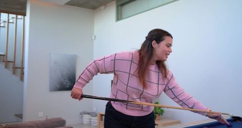 Young woman aiming cue on blue pool table in modern minimalist home game room