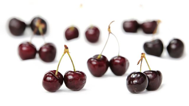 Image of fresh sweet cherries scattered on a white background. Perfect for use in advertisements, food blogs, recipe books, or health-related content to signify freshness, natural produce, and vibrant nutrition.