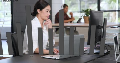 Focused businesswoman typing at open-plan office with transparent bar chart overlay