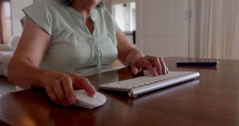 Senior woman typing on wireless keyboard in home office setting