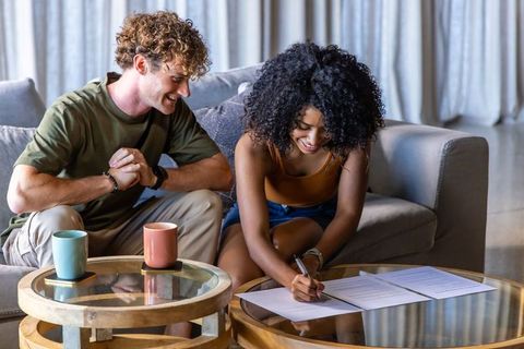 Young couple signing rental agreement on glass coffee table, cozy living room