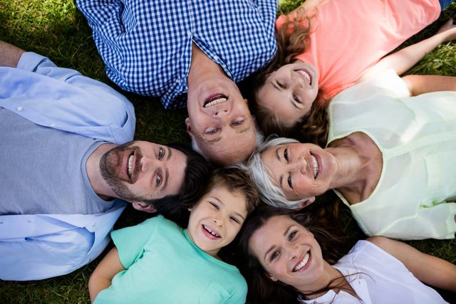 Multi-generation family lying on grass in a circle, smiling and bonding. Ideal for concepts of family unity, togetherness, and outdoor leisure. Perfect for advertisements, family-oriented content, and lifestyle blogs.
