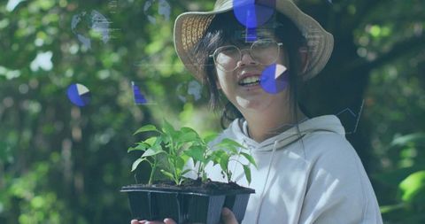 Young girl holding seed tray wearing straw hat, glasses tending seedlings with hud overlay