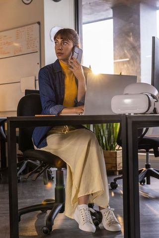 Businesswoman balancing phone communication and laptop work at modern office