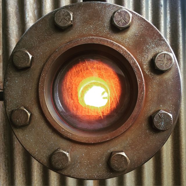 Closeup of a circular industrial observation window showcasing a glowing light within. Ideal for use in themes concerning engineering, steampunk aesthetics, industrial design, and machinery inspections. Great visual representation for technological and mechanical presentations, articles, blog posts, or steampunk art projects.