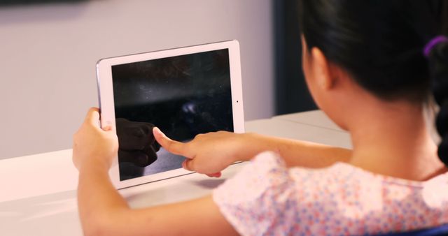 Young girl in braids interacting with a tablet in a modern classroom. Perfect for illustrating concepts of digital education, interactive learning, and the integration of technology in schools. Ideal for use in educational publications, technology advertisements, and online learning platforms.