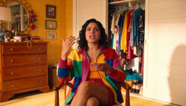 Confident woman speaking and gesturing in colorful rainbow jacket sitting in cozy bedroom