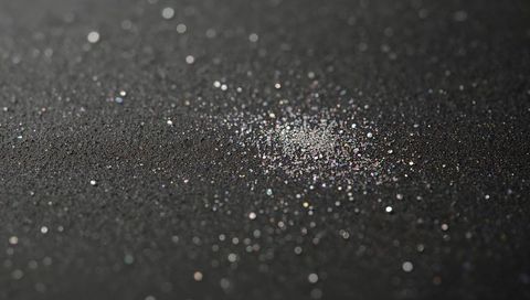Iridescent glitter specks scattering on dark rough surface with soft bokeh macro texture
