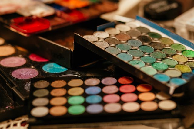 Close-up view of various colorful makeup palettes and brushes on a vanity table. Ideal for use in beauty, fashion, cosmetic advertisements, makeup tutorials, and personal care promotions.