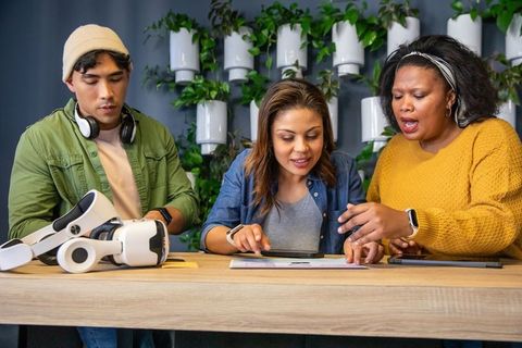 Diverse team collaborating on vr headset and tablet in modern green office workspace