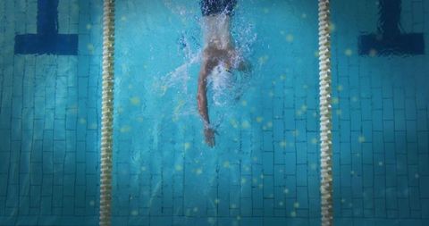 Overhead diving male swimmer gliding through pool lane with splash and trailing bubbles