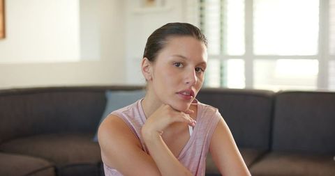 Contemplative woman resting chin on hand in modern living room with natural light