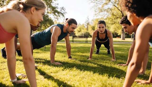Group training doing planks in park circle, woman holding high plank, outdoor fitness
