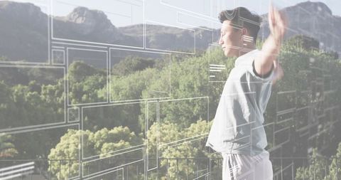 Asian man raising arms on balcony using futuristic UI overlays over mountain landscape