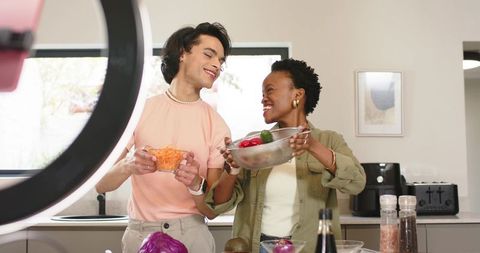 Happy couple preparing colorful salad on kitchen counter with ring light for cooking video