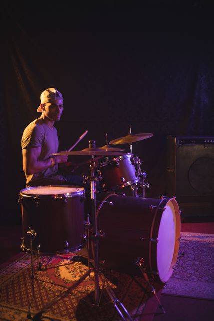 Confident male performing with drum kit in illuminated nightclub