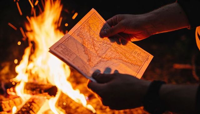 Holding unfolded map by campfire at night for camping navigation and outdoor adventure