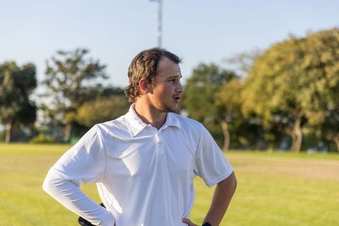 Man standing on sunlit grassy field wearing white polo and wristwatch looking to side