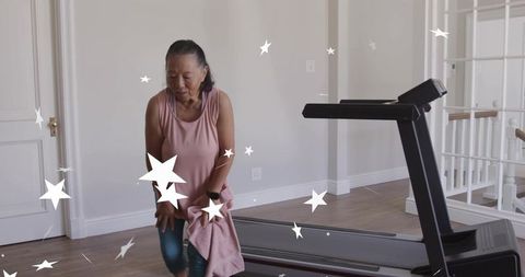 Senior woman pausing treadmill workout at home holding towel and wearing smartwatch