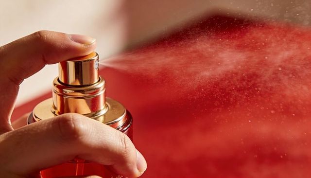 Golden luxury perfume spray creating fine mist over red background glass bottle close-up