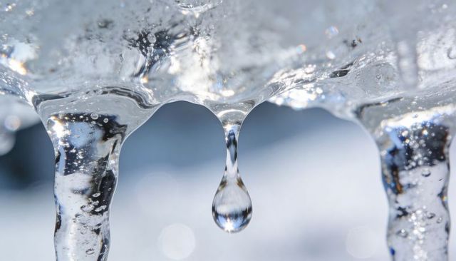 Dripping icicle with suspended droplet, crystalline ice texture and sunlit macro